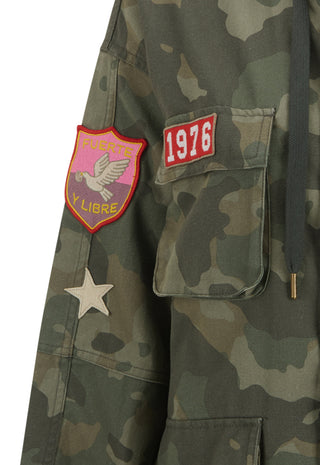 Close-up of a camouflage jacket with a pink and yellow  patch, a red '1976' patch, and a white star patch on the sleeve.
